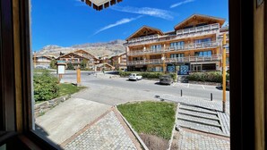 A view of a hotel with multiple wooden balconies, a parking area, and a mountain backdrop. - Résidence la Ménandière W1 (Alpe d'Huez)