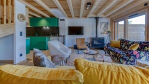 A modern living room with a wooden ceiling, a green kitchen, a fireplace, and a sofa with a colorful floral pattern. - Duplex Résidence de l'Alpe (Alpe d'Huez)