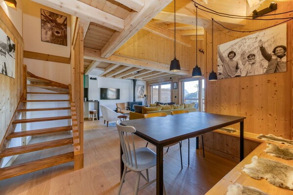 A spacious room with a wooden staircase, a dining table, and a sofa.