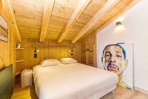 A wooden cabin room with a bed, a wall-mounted light, and a painting.