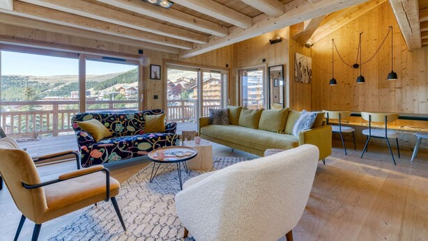 A spacious living room with wooden beams, a sofa, chairs, a coffee table, and a view of the mountains. - Duplex Résidence de l'Alpe (Alpe d'Huez)