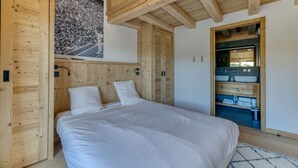 A bedroom with a wooden headboard, a bed with white bedding, a wooden wardrobe, and a bathroom with a mirror and sink. - Duplex Résidence de l'Alpe (Alpe d'Huez)