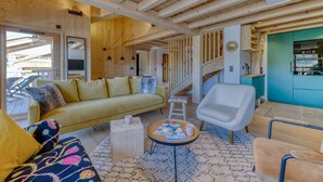 A cozy living room with a sofa, armchair, and coffee table, wooden beams on the ceiling, and a staircase leading to another level. - Duplex Résidence de l'Alpe (Alpe d'Huez)