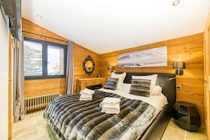 Un dormitorio con pared de madera, una cama con manta a rayas, una mesita de noche, un espejo y un cuadro en la pared.
