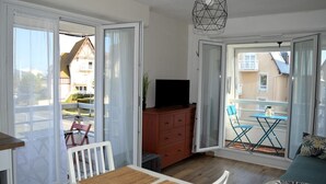 A room with a dining table, a TV on a cabinet, and a balcony with a table and chairs. - Le petit Courseulles - between port and sea (Courseulles-sur-Mer)