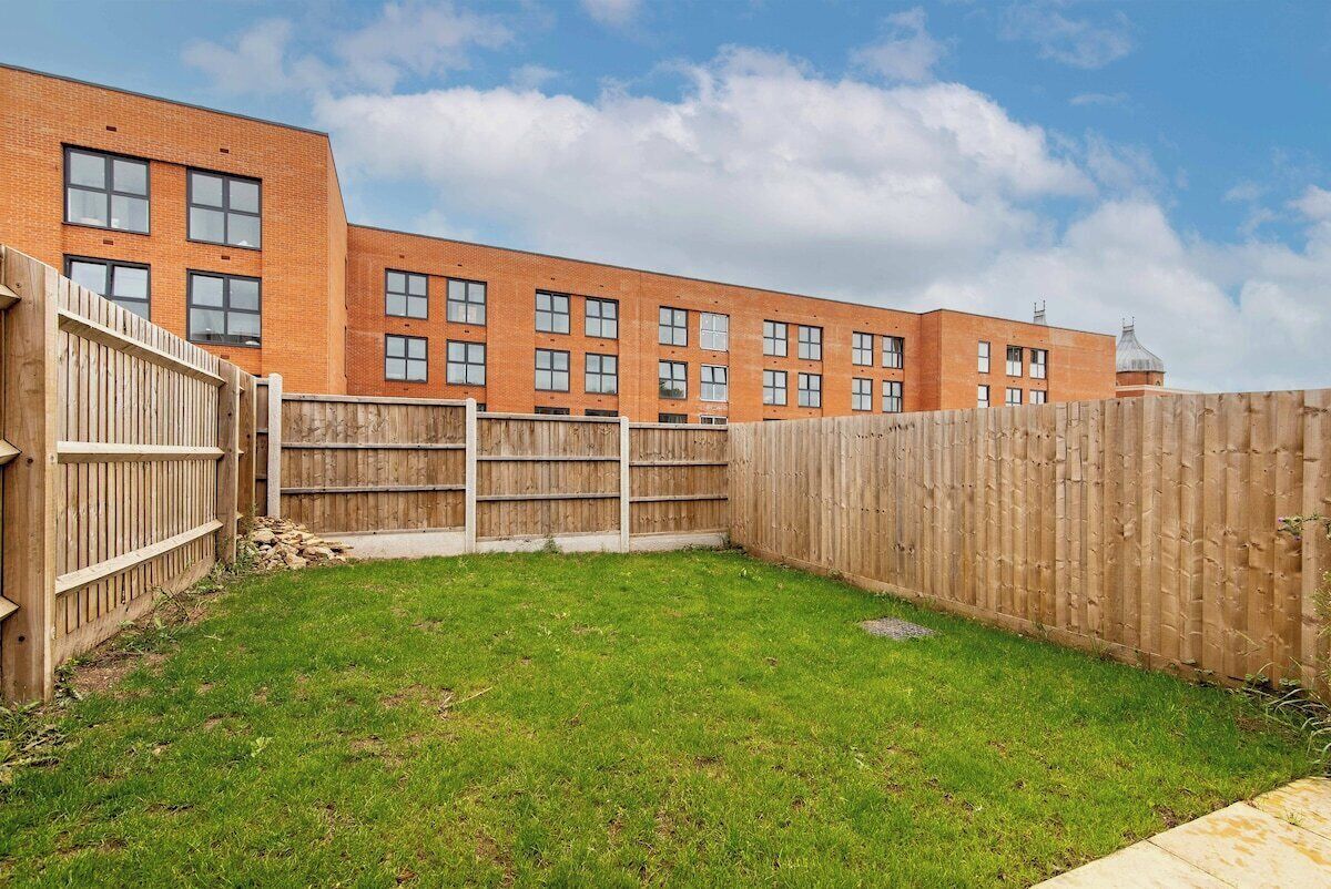 A fenced backyard with a grassy area and a brick building in the background.
