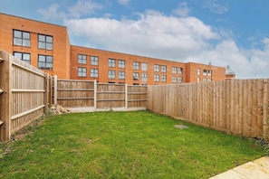 A fenced backyard with a grassy area and a brick building in the background.