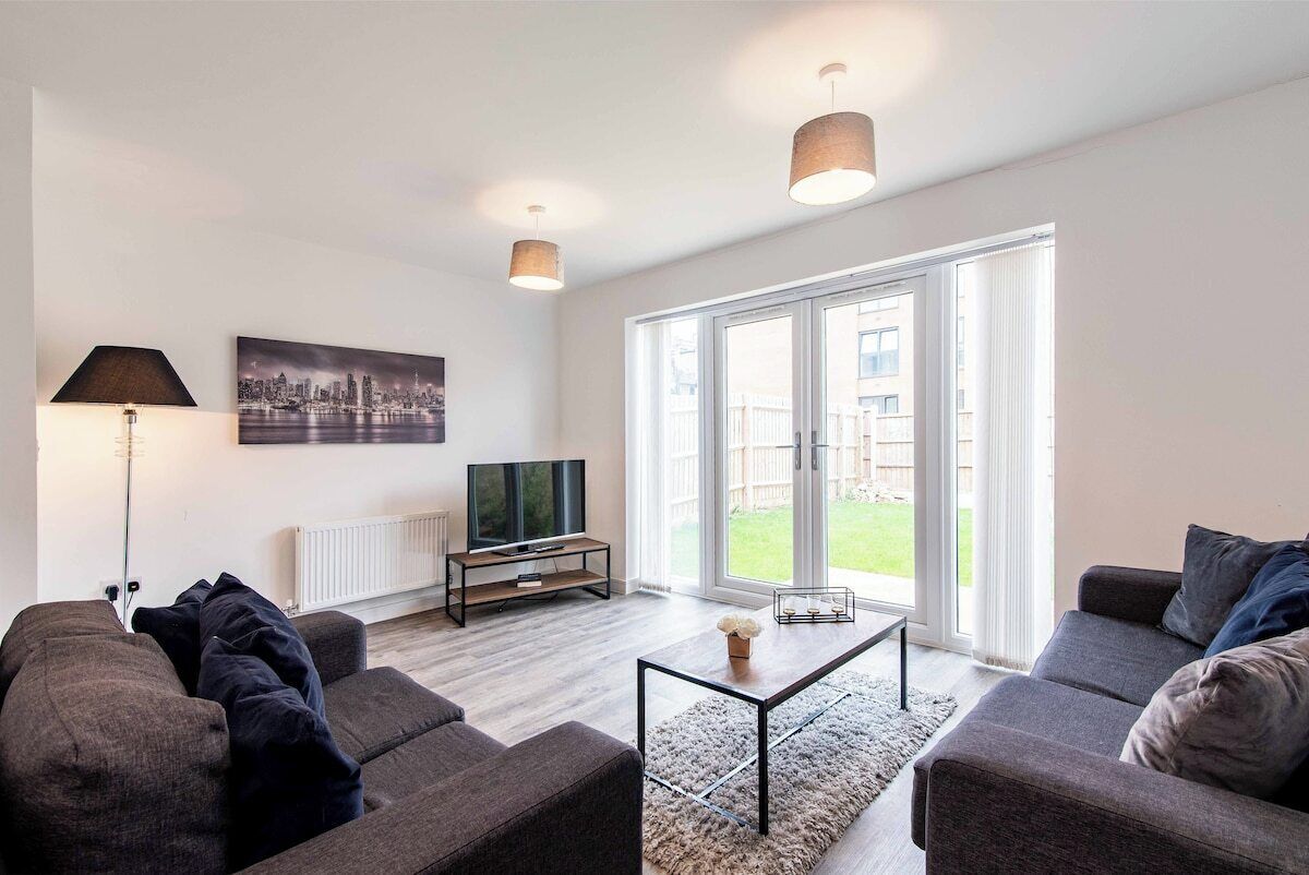 A modern living room with a sofa, a coffee table, a TV, and a large window with a view of the outdoors.