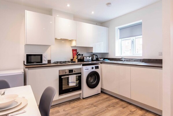 A compact kitchen with white cabinets, a microwave, a stove, a washing machine, and a window.