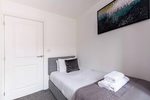 A hotel room with a bed, a door, and a painting on the wall.