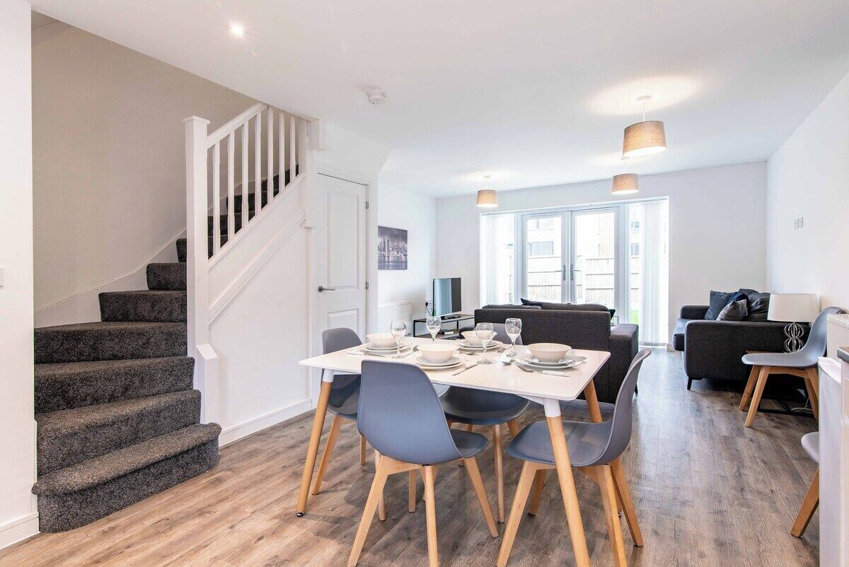 A modern dining area with a staircase, a dining table set for four, and a living area with a sofa and a lamp.