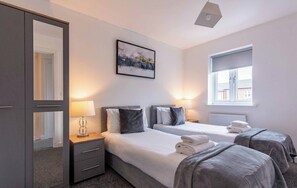 A hotel room with two beds, a wardrobe, a painting on the wall, and a window with a view.