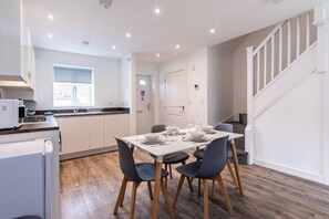 A modern kitchen with white cabinets, a dining table set for four, and a staircase leading to an upper level.