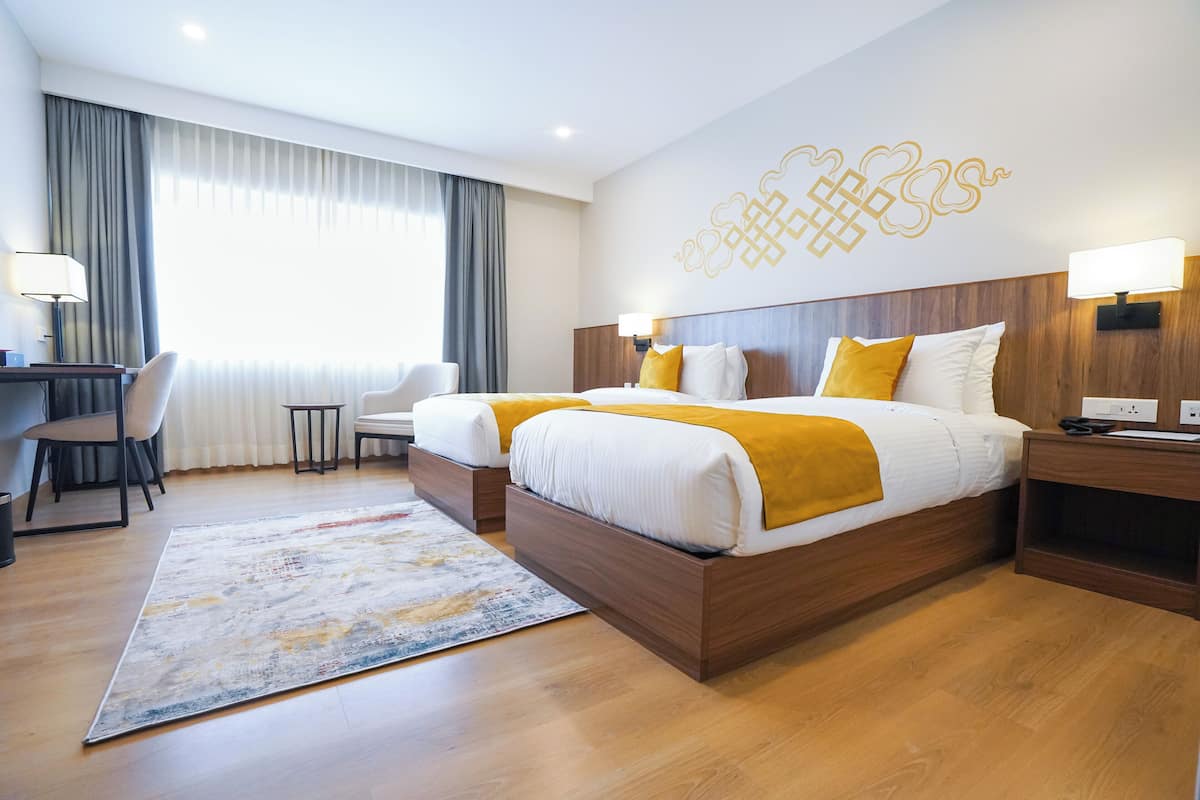 Ein Hotelzimmer mit zwei Betten, einem Schreibtisch, einem Stuhl und einem großen Fenster mit Vorhängen.