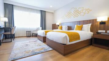 Habitación de hotel con dos camas, un escritorio, una silla y un amplio ventanal con cortinas.