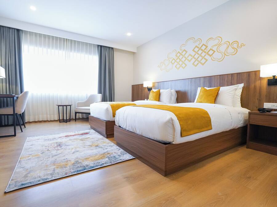 Habitación de hotel con dos camas, un escritorio, una silla y un amplio ventanal con cortinas.