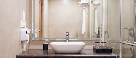 Un baño moderno con un espejo grande, un lavabo blanco y una ducha con mampara de vidrio.
