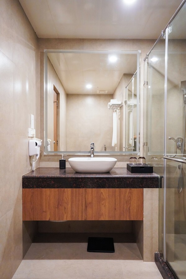 A modern bathroom with a large mirror, a white sink, and a glass-enclosed shower. - The Capital Hotel Thimphu (Thimphu)