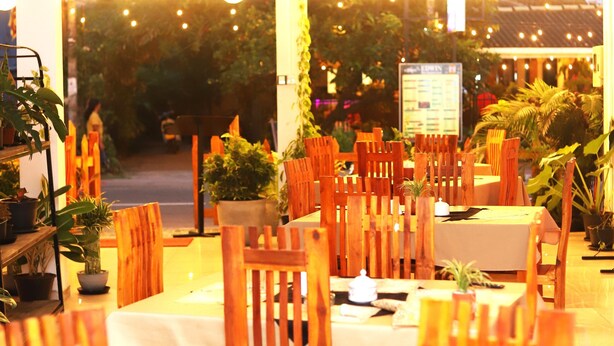 A restaurant with wooden tables and chairs, hanging plants, and string lights. - Royal Hub (Negombo)
