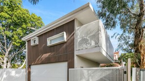 Une maison moderne à deux étages, dotée d’un garage, d’un balcon et d’une allée d’accès fermée par un portail.