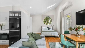 Une chambre à coucher moderne et bien éclairée, avec un lit, une fenêtre ronde et un coin repas comprenant une table et des chaises.