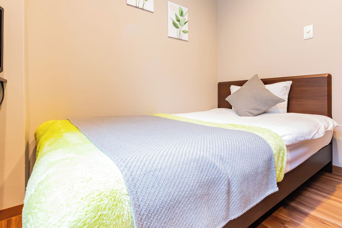 A single bed with a wooden headboard, a yellow and white blanket, and a grey pillow.