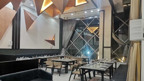 Un espace de repas moderne avec des tables et des chaises, un canapé noir et une grande fenêtre avec des rideaux.