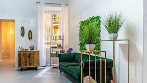 Una sala de estar moderna con un sofá verde, un aparador dorado y una planta alta sobre un pedestal dorado.