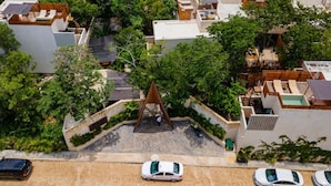 An aerial view of a residential area with multiple buildings, a central triangular structure, and parked cars. - Luxury 2BR Villa with Private Pool, Spacious Living & Modern Amenities (Tulum)