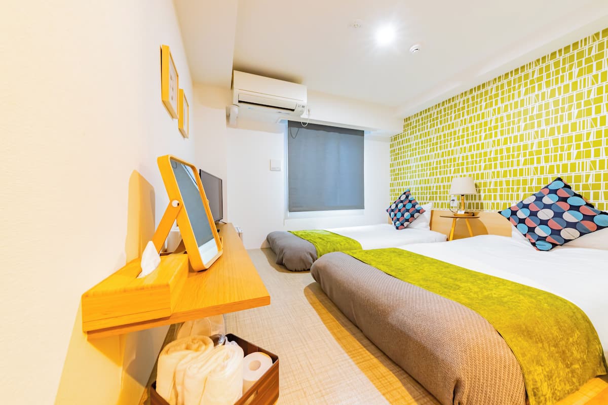 A hotel room with a bed, a desk with a computer, an air conditioner, and a window with a curtain.