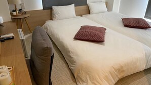 Una habitación de hotel con dos camas, un escritorio con lámpara y una pequeña mesa con una planta.