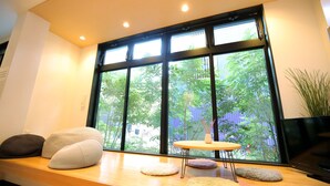 Una habitación moderna con un ventanal grande, una mesa redonda y varios cojines en un banco de madera.