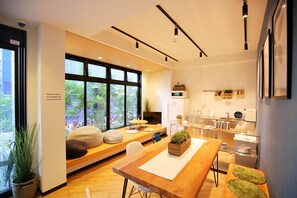 A modern hotel room with a large window, a wooden dining table, a sofa with cushions, a kitchen area, and a small balcony. - JA Hotel Midoribashi (Osaka)