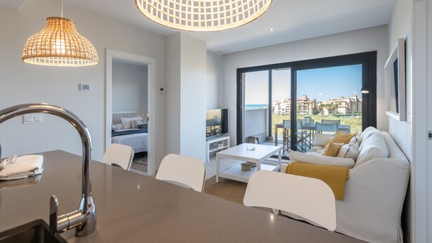 En moderne stue med sofa, sofabord og spiseplads. Et stort vindue giver udsigt over byen.