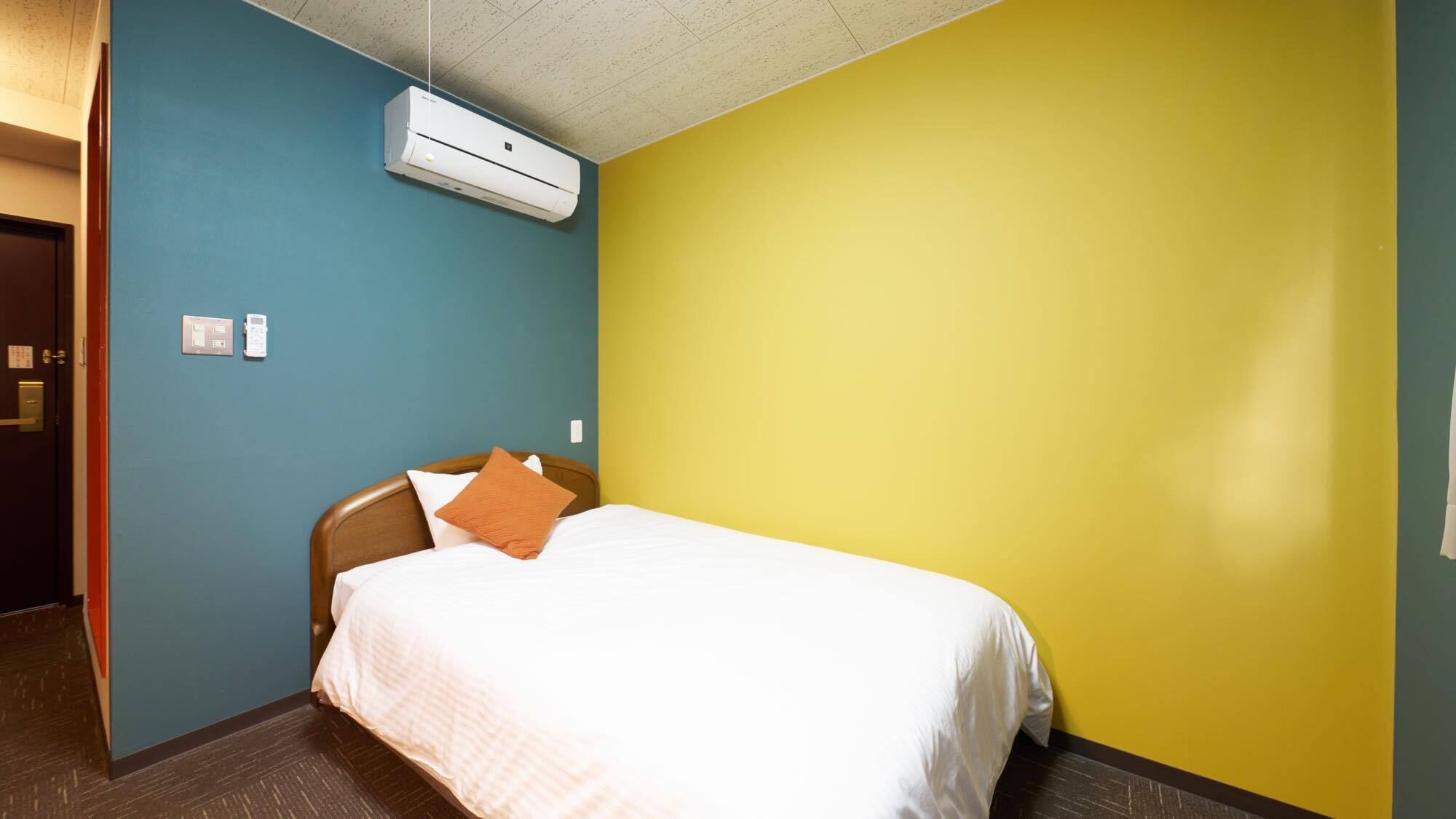 A hotel room with a bed, a wall-mounted air conditioner, and a door.