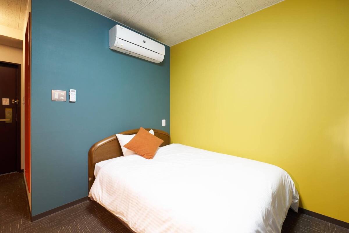 A hotel room with a bed, a wall-mounted air conditioner, and a door.