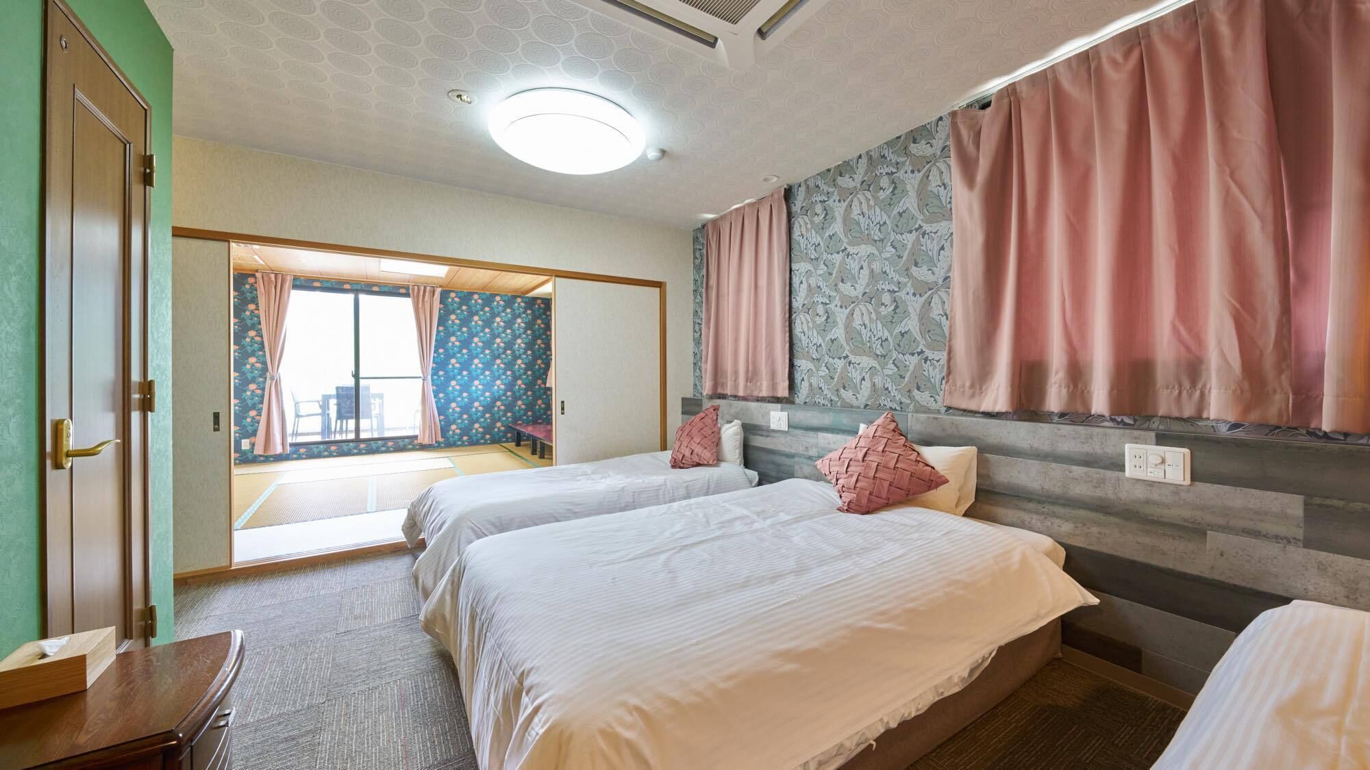 A hotel room with two beds, a wooden desk, a large window with curtains, and a patterned wall.