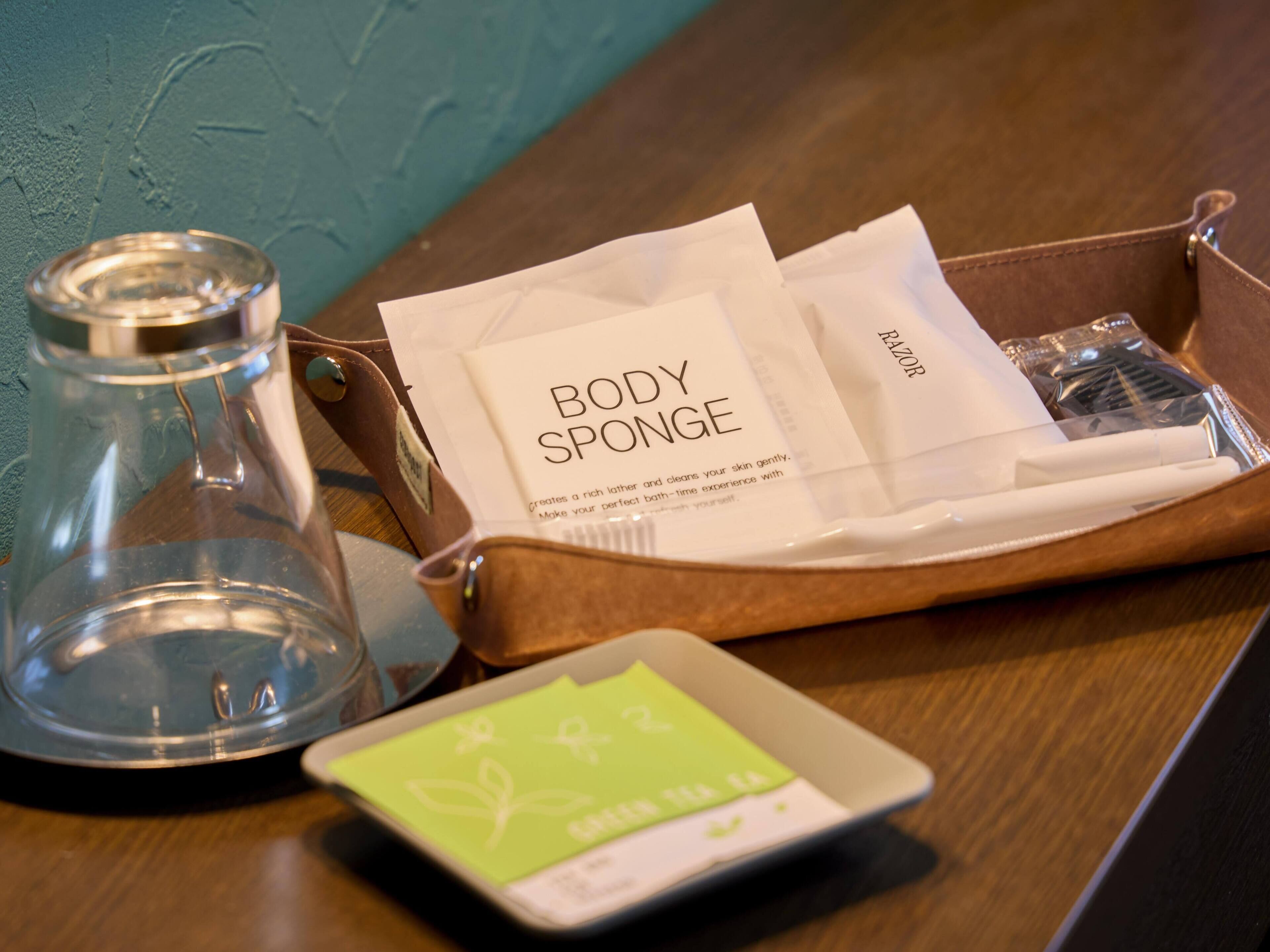 A bathroom with a glass jar, a brown leather toiletry bag containing a body sponge, razors, and a small green card.
