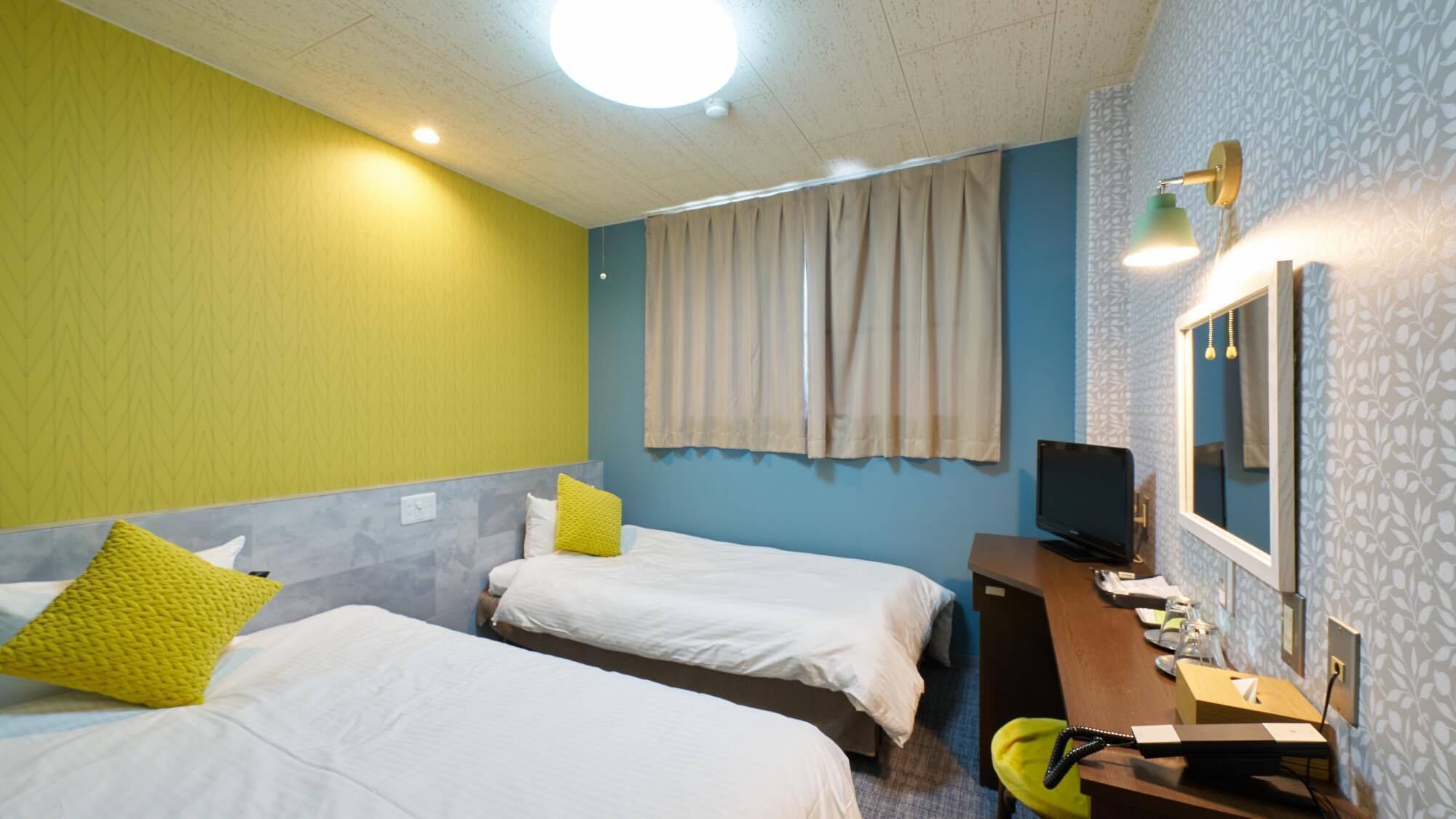 A hotel room with two beds, a desk with a computer, a TV, and a window with curtains.