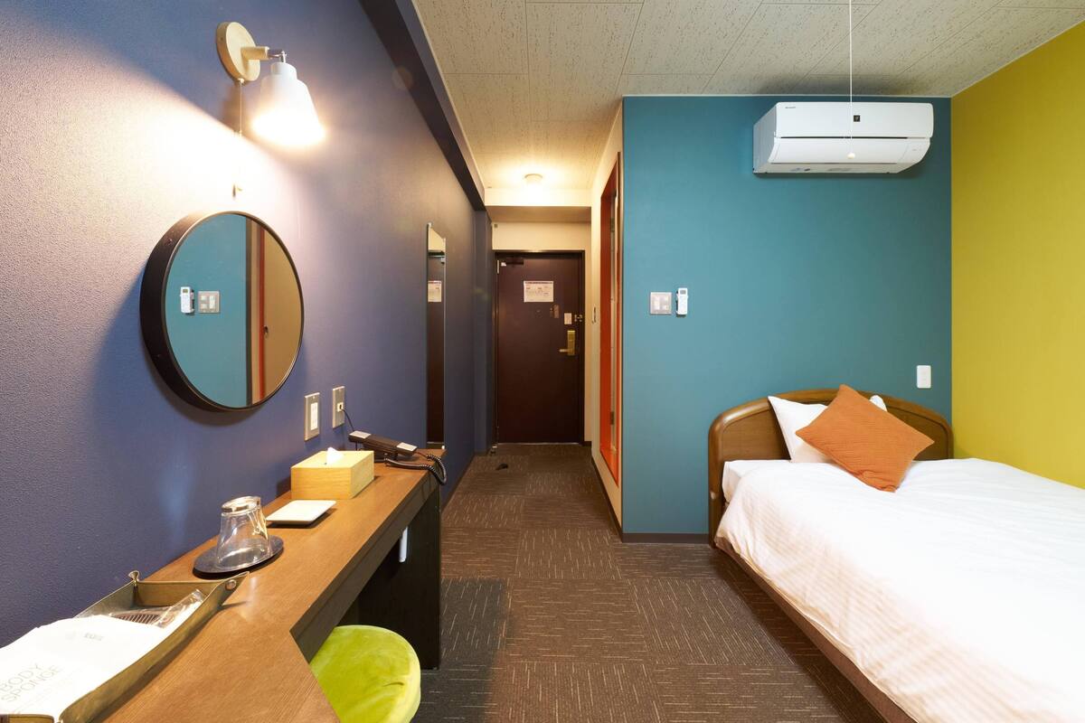 A hotel room with a bed, bedside table, mirror, and a wall-mounted air conditioner.