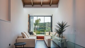 A modern living room with a sofa set, a glass table, and a view of a lush landscape through large windows. - Casa del Balo - Harmony in Nature by etouri (Chania)