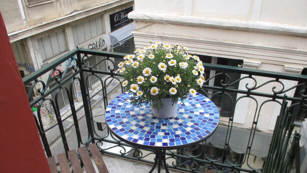 Un balcón con una mesa de mosaico, una maceta con una margarita y bancos de madera.