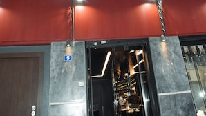 Un edificio rojo con balcón, unidades de aire acondicionado y entrada a una tienda.