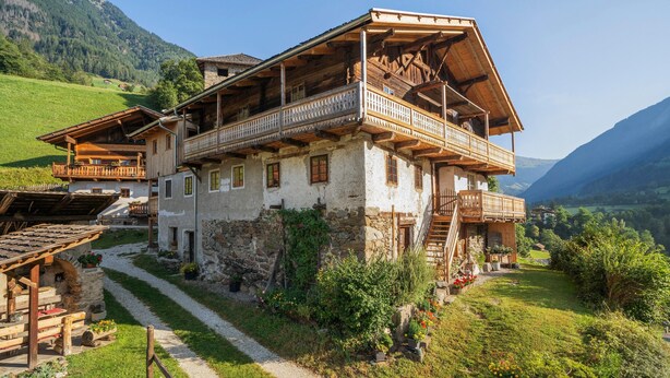 Ein traditionelles Holzchalet mit Balkon, Steinmauern und einem Kiesweg zum Eingang.