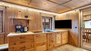 Ein Holzinnenraum mit Küchenzeile, inklusive Kaffeemaschine, Spüle und einem an der Wand montierten Fernseher.