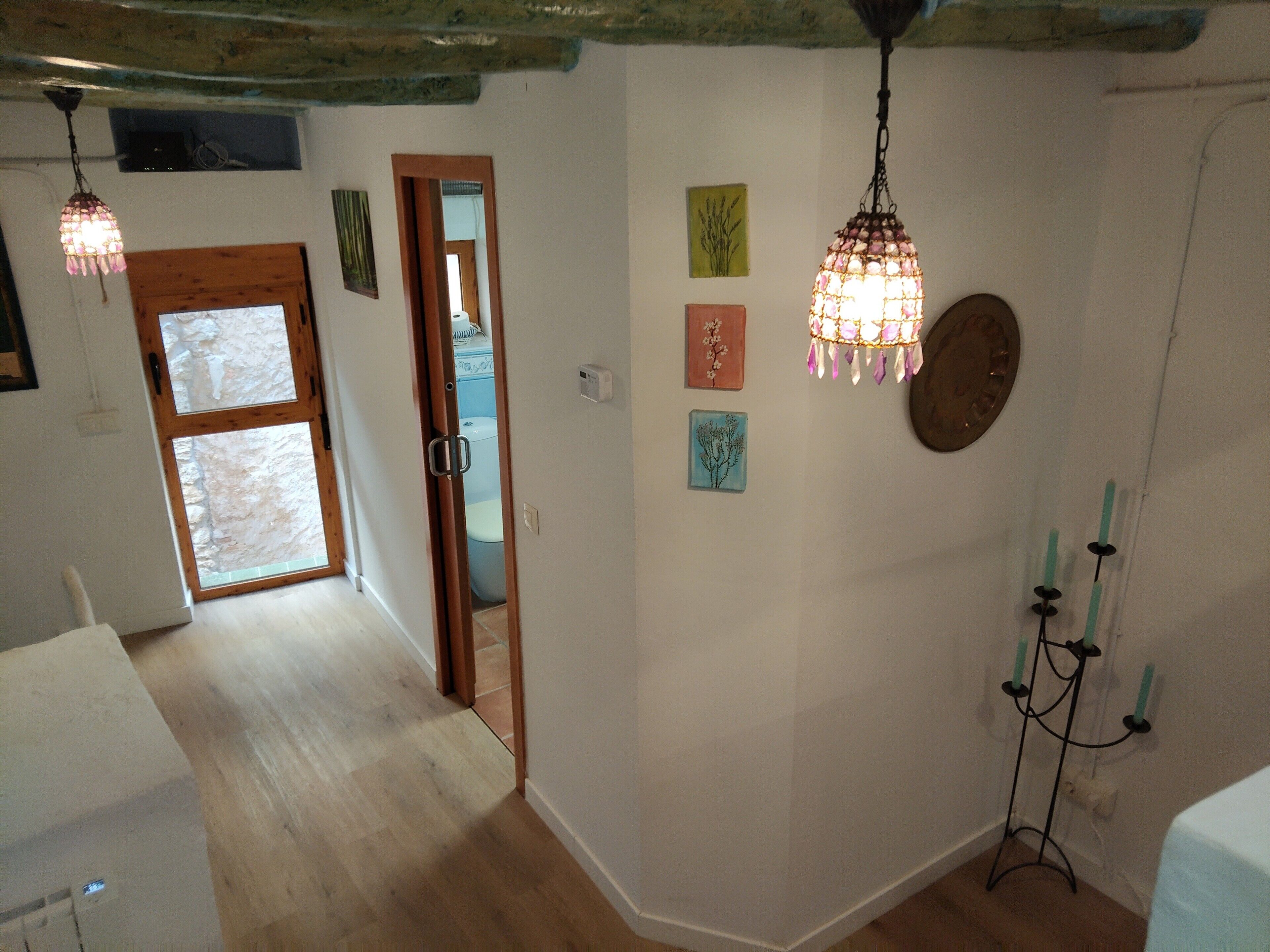 Una habitación con piso de madera, una puerta de madera, una ventana y obras de arte colgadas en la pared.
