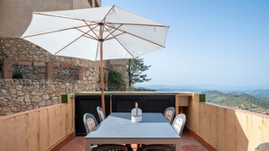 Une terrasse avec une table et des chaises, un parasol blanc et une vue sur le paysage.