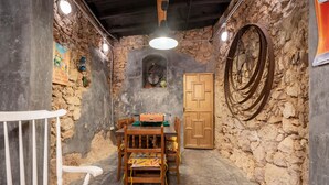 Une pièce rustique aux murs de pierre, avec une table à manger en bois, des chaises et une petite fenêtre.