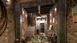 Une pièce avec une table de baby-foot, des murs en pierre, un escalier et un plafond orné d’objets suspendus.