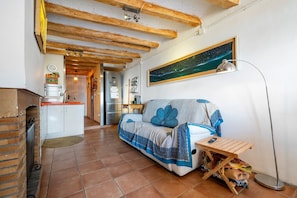 A cozy living area with a sofa, a small table, a floor lamp, and a kitchen in the background. - Vacation Home "Cal Cosials" with Mountain View, Private Terrace & Balcony (La Morera de Montsant)